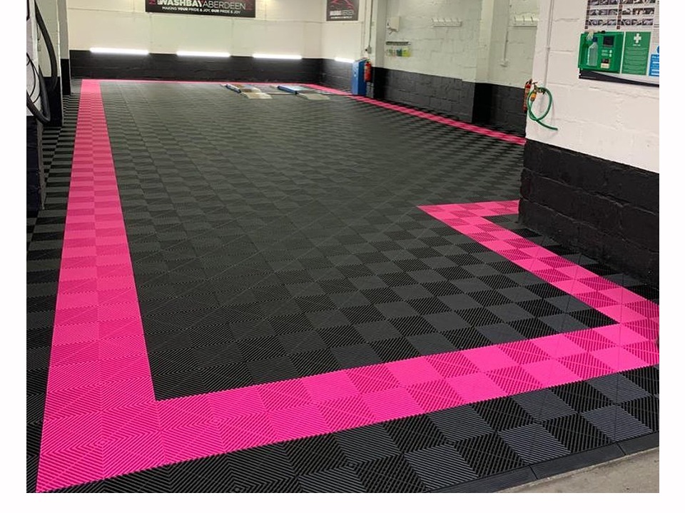Black interlocking garage floor tiles with a bright pink border laid in a car wash bay